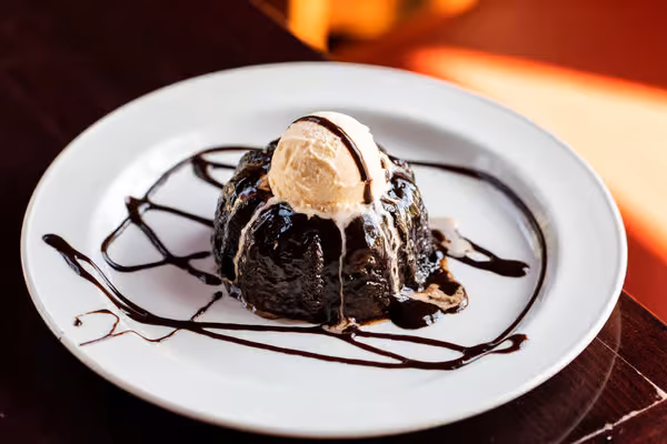 Chocolate cake with vanilla ice cream and chocolate sauce on a white plate.