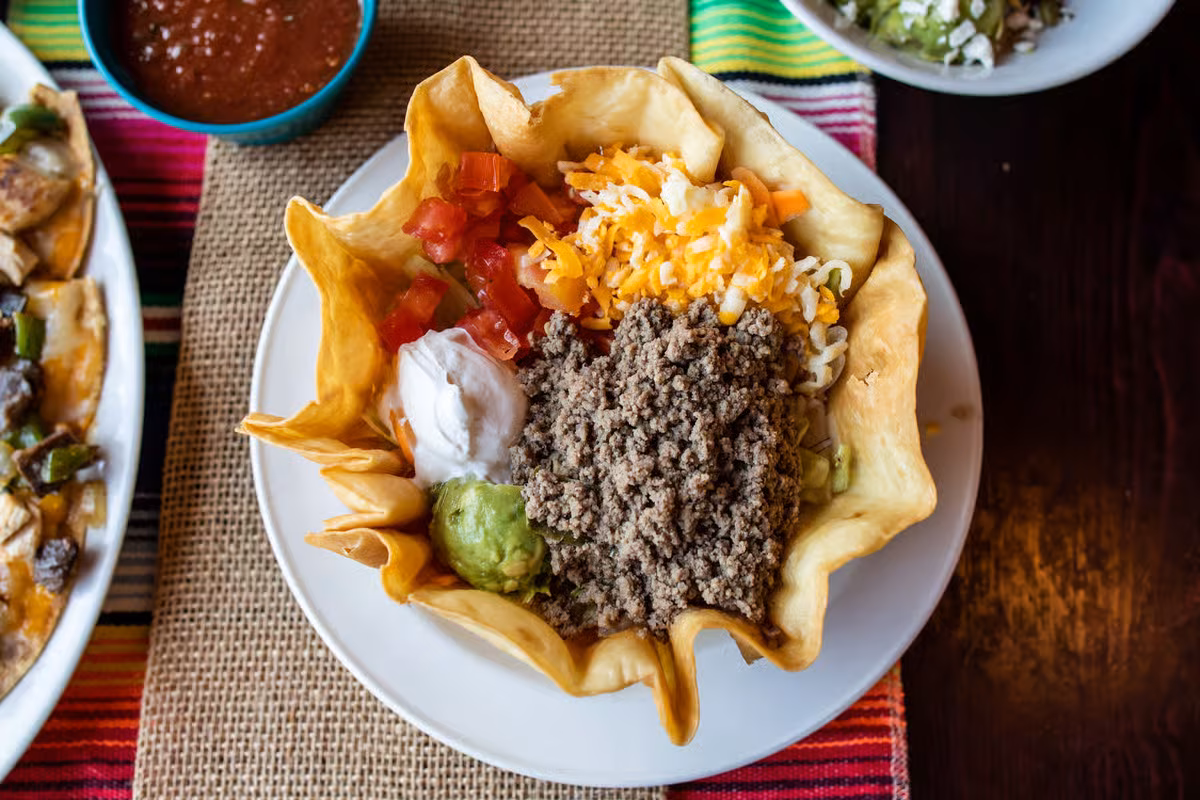 Taco salad in a crispy tortilla bowl with ground beef and toppings.