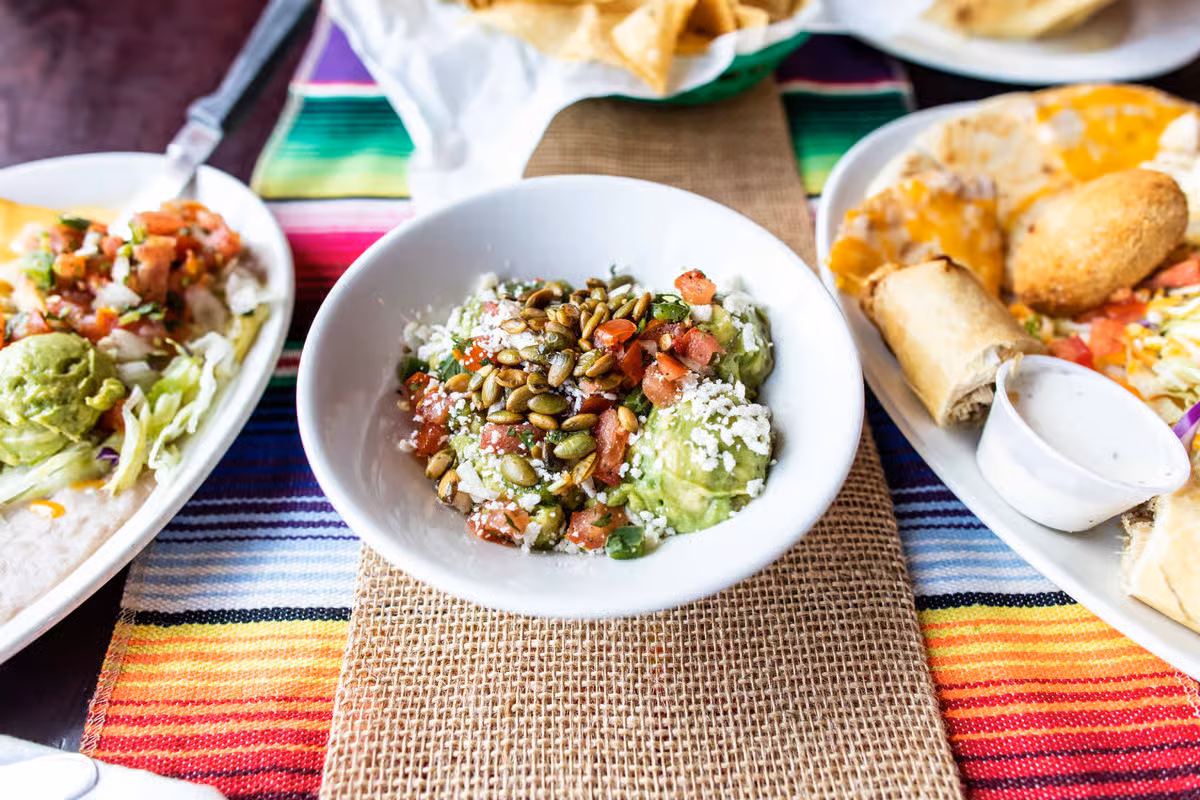 Table spread with various Mexican dishes, including guacamole and quesadillas.
