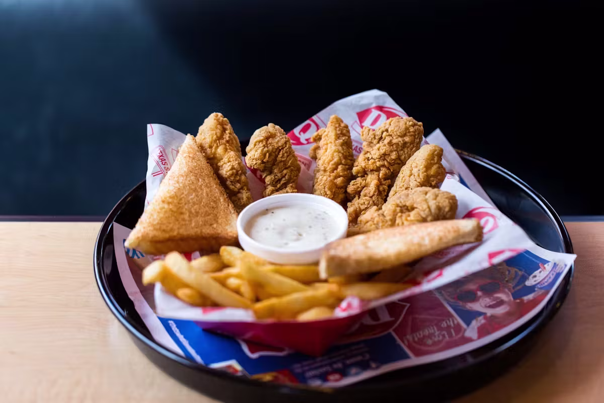 Fried chicken strips, french fries, toast, and dipping sauce in a bowl.