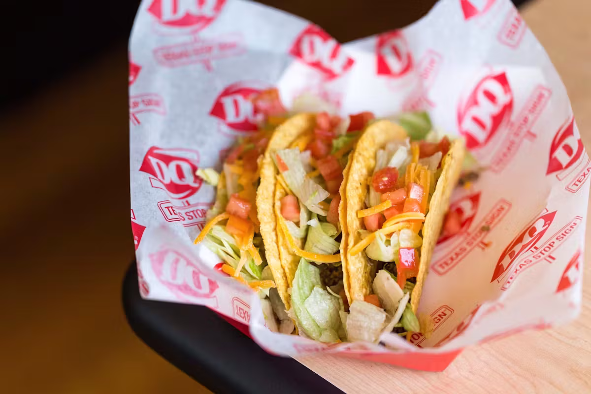 Three hard-shell tacos with lettuce, cheese, and tomatoes in DQ wrapper.