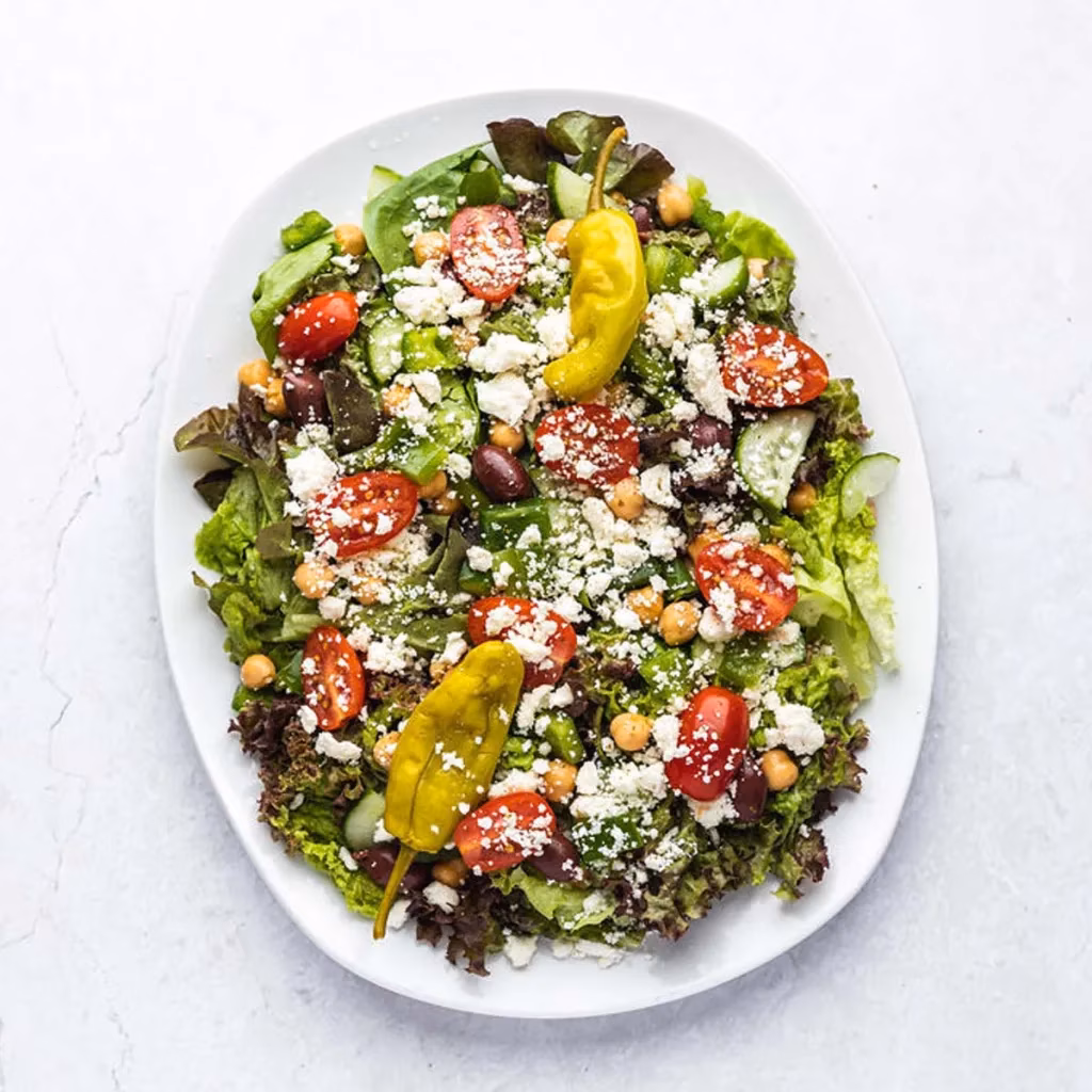 Large salad with mixed greens, tomatoes, feta, olives, chickpeas, and pepperoncini.