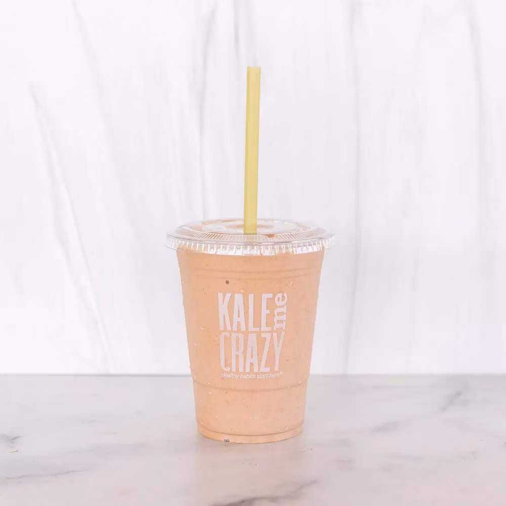 Orange smoothie in a 'Kale Me Crazy' branded cup with a yellow straw.