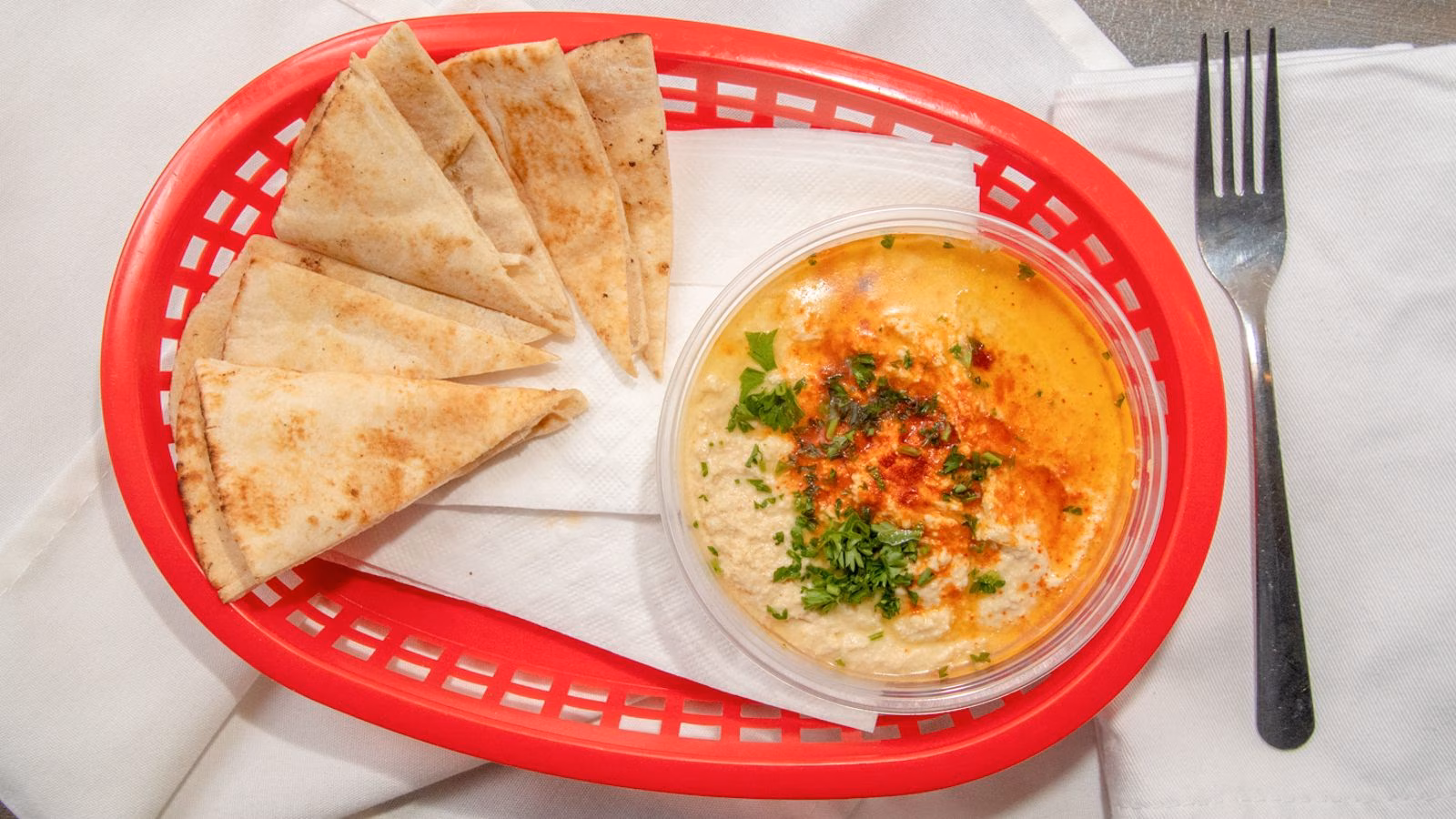 Pita bread and hummus in a red basket with a fork.