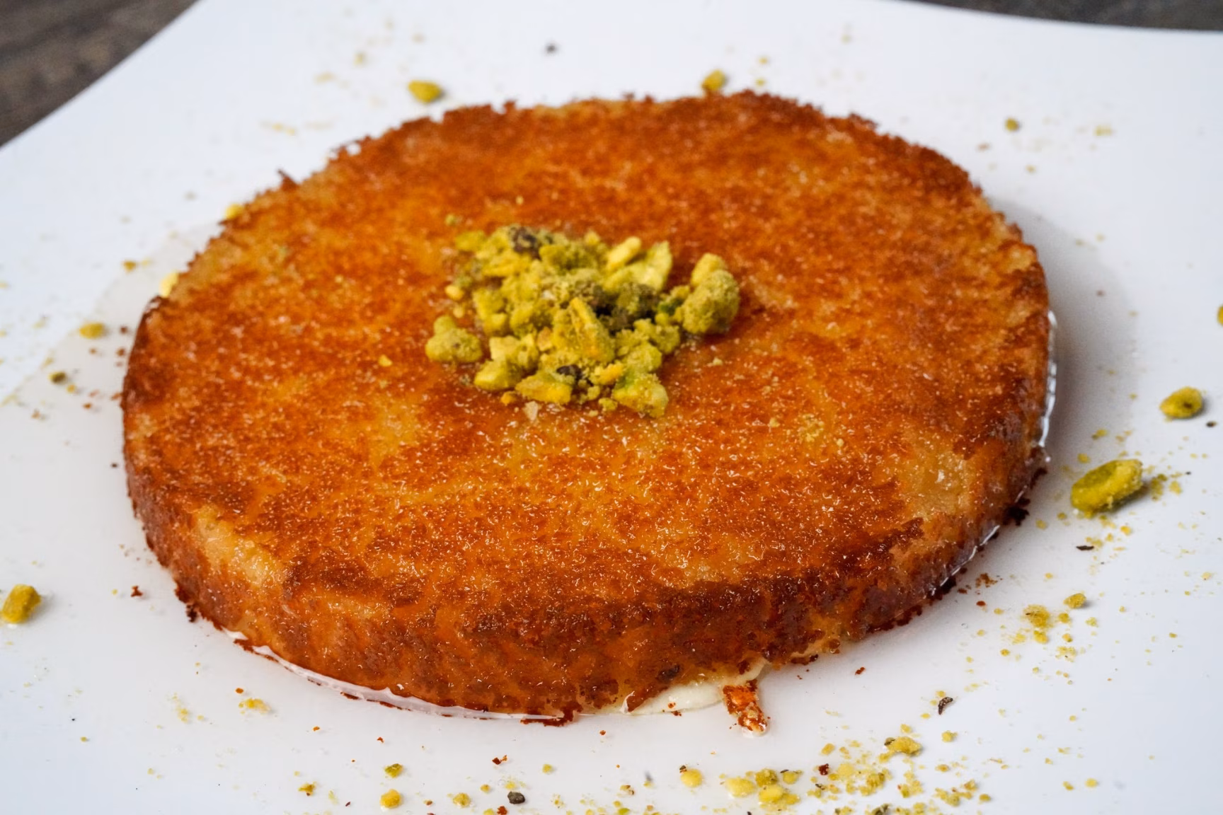 Golden-brown dessert topped with chopped pistachios on a white plate.