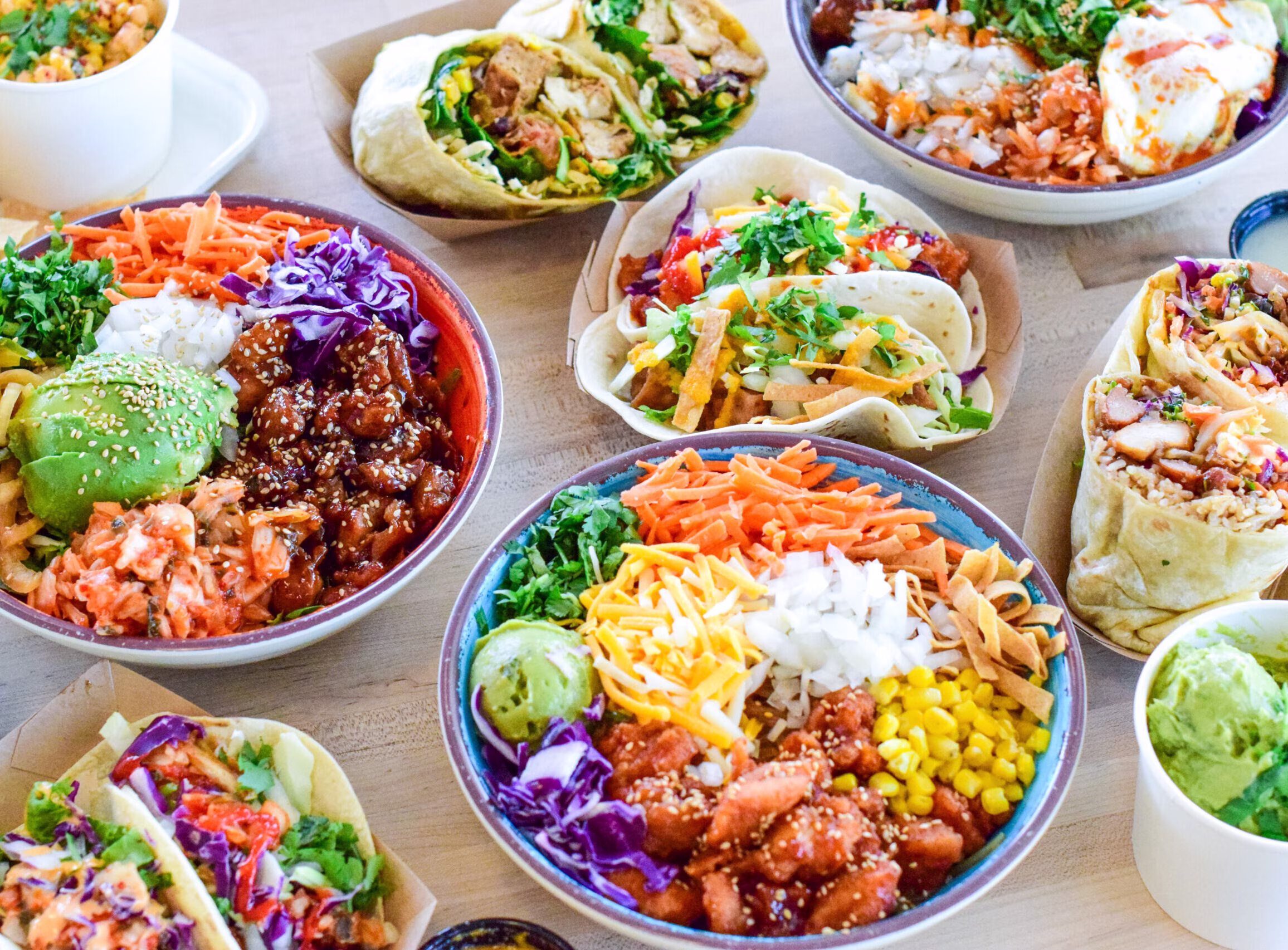 A variety of colorful bowls, burritos, and tacos on a table.