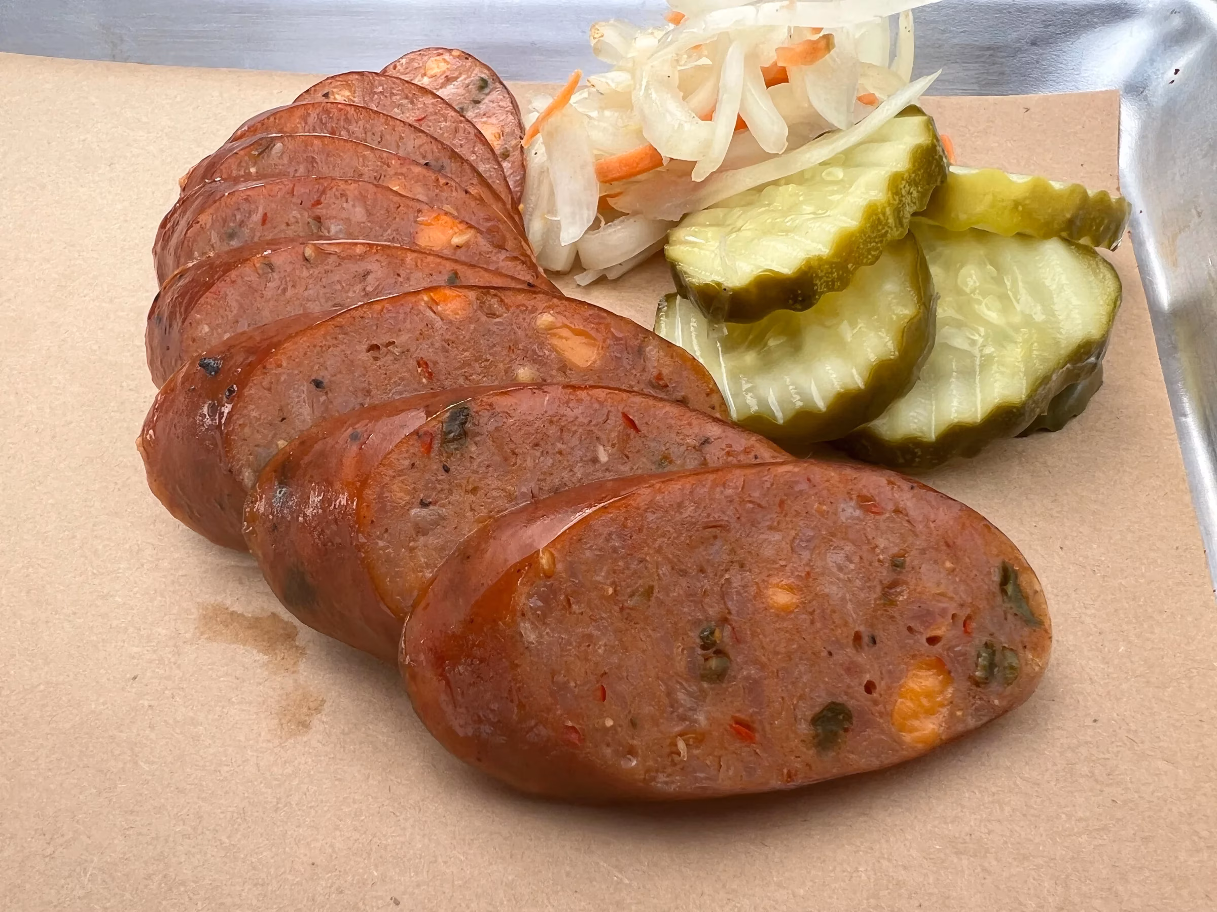 Smoked sausage slices, dill pickles, and pickled vegetables on paper.
