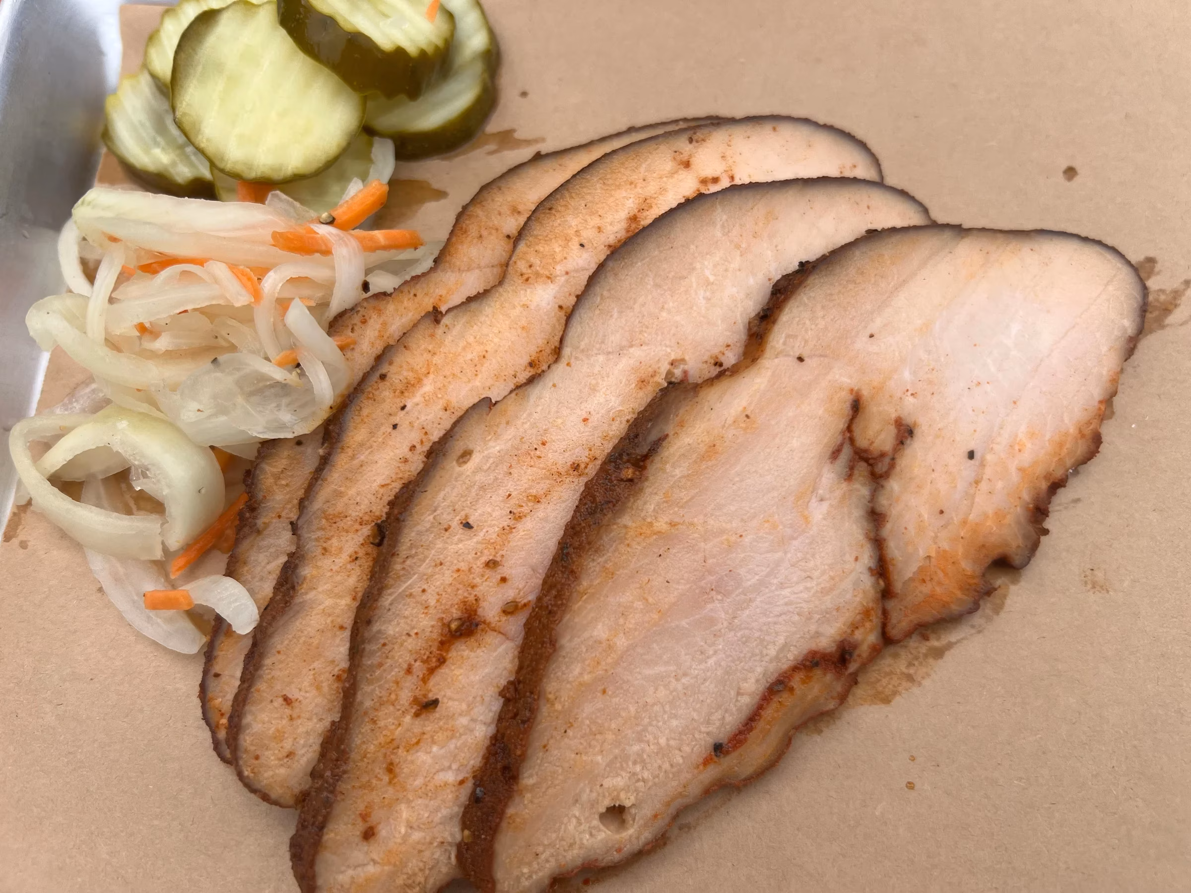 Slices of cooked meat, cucumber pickles, and sliced onion with carrots.