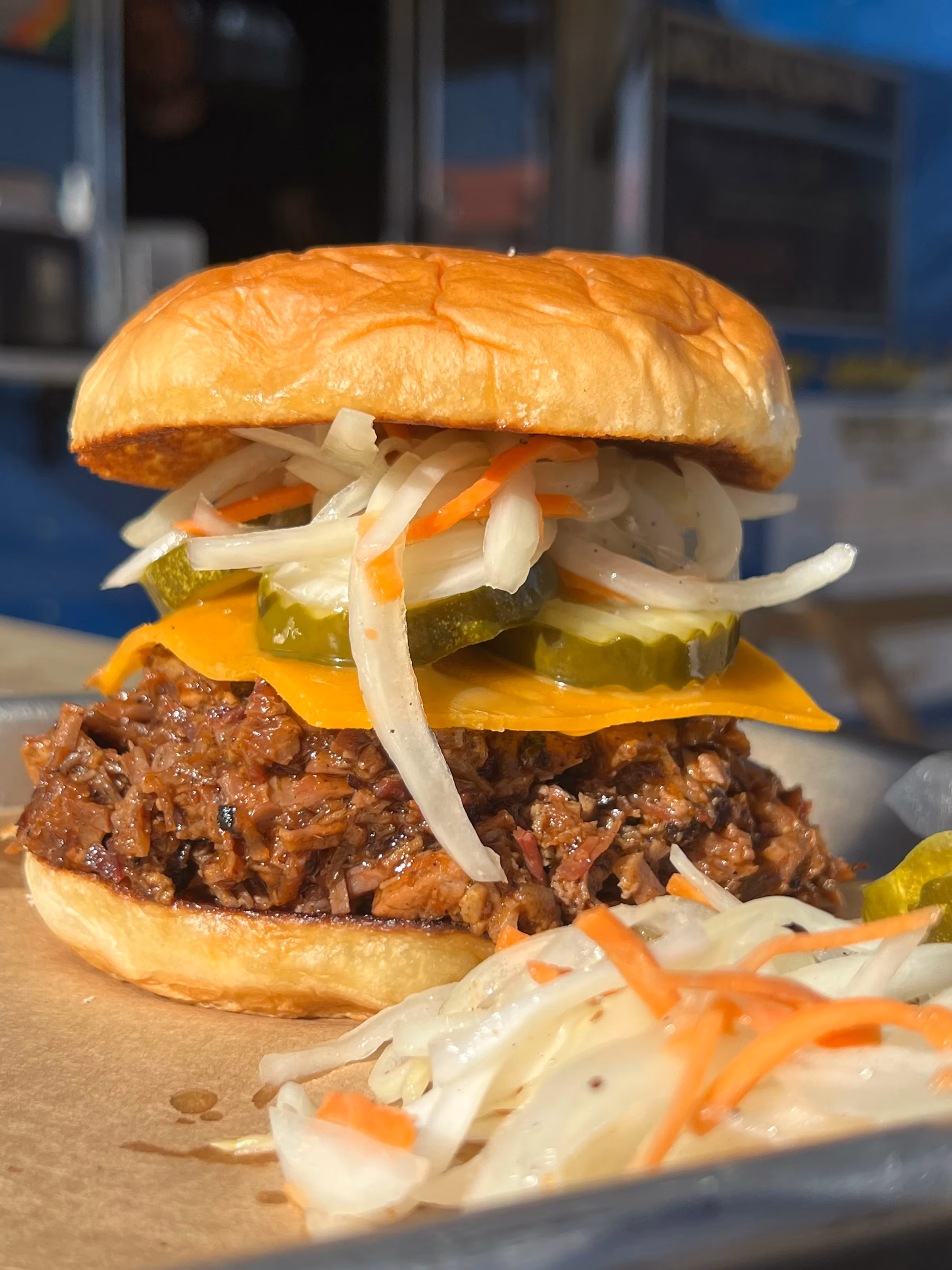 Pulled meat sandwich with cheese, pickles, and coleslaw.
