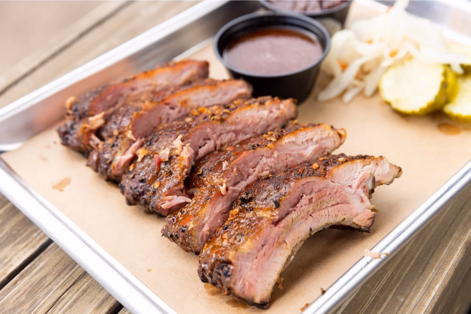 Sliced barbecue ribs with sauce, pickles, and onions on a tray.