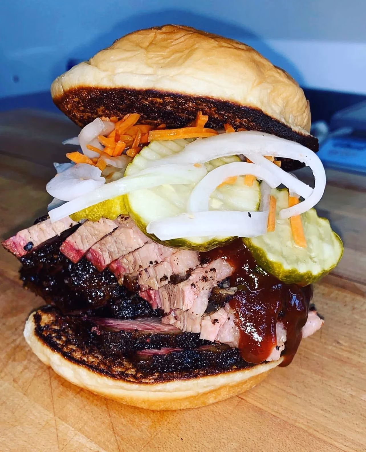 Brisket sandwich with pickles, onions, carrots, and barbecue sauce.