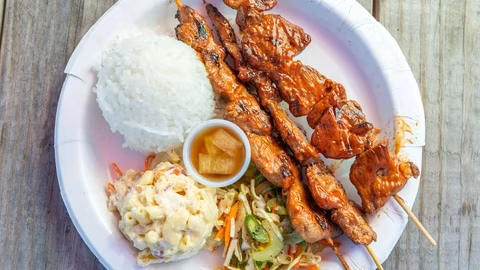 White plate with grilled skewers, rice, macaroni salad, and vegetable slaw.
