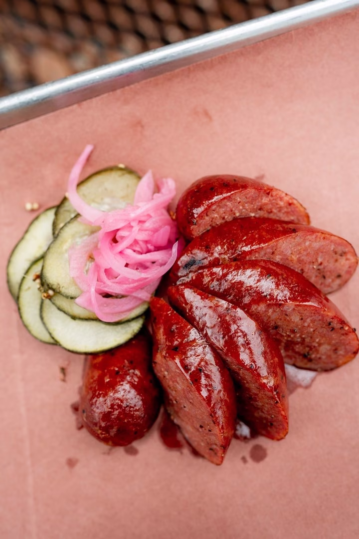 Sliced sausages with pickled cucumbers and pink onions on paper.