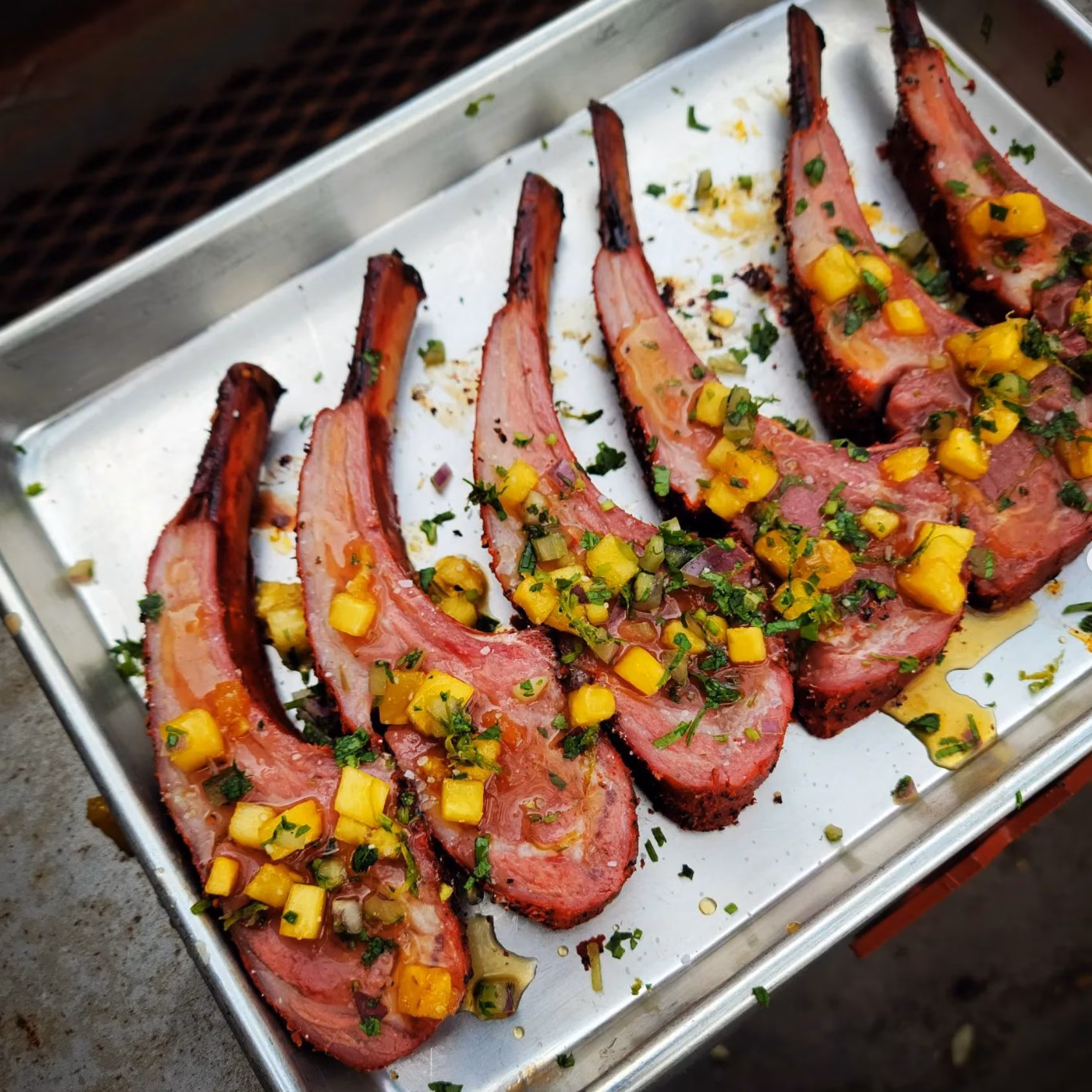 Six cooked chops topped with mango salsa on a metal tray.
