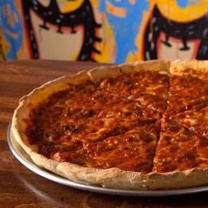 A deep-dish pizza with thick red sauce on a pan, colorful background.