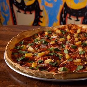 Pizza topped with pineapple, pepperoni, and fresh cilantro on a wooden table.