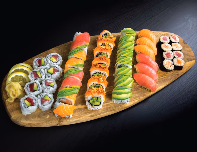 Assortment of sushi rolls, nigiri, ginger, and lemon on a board.