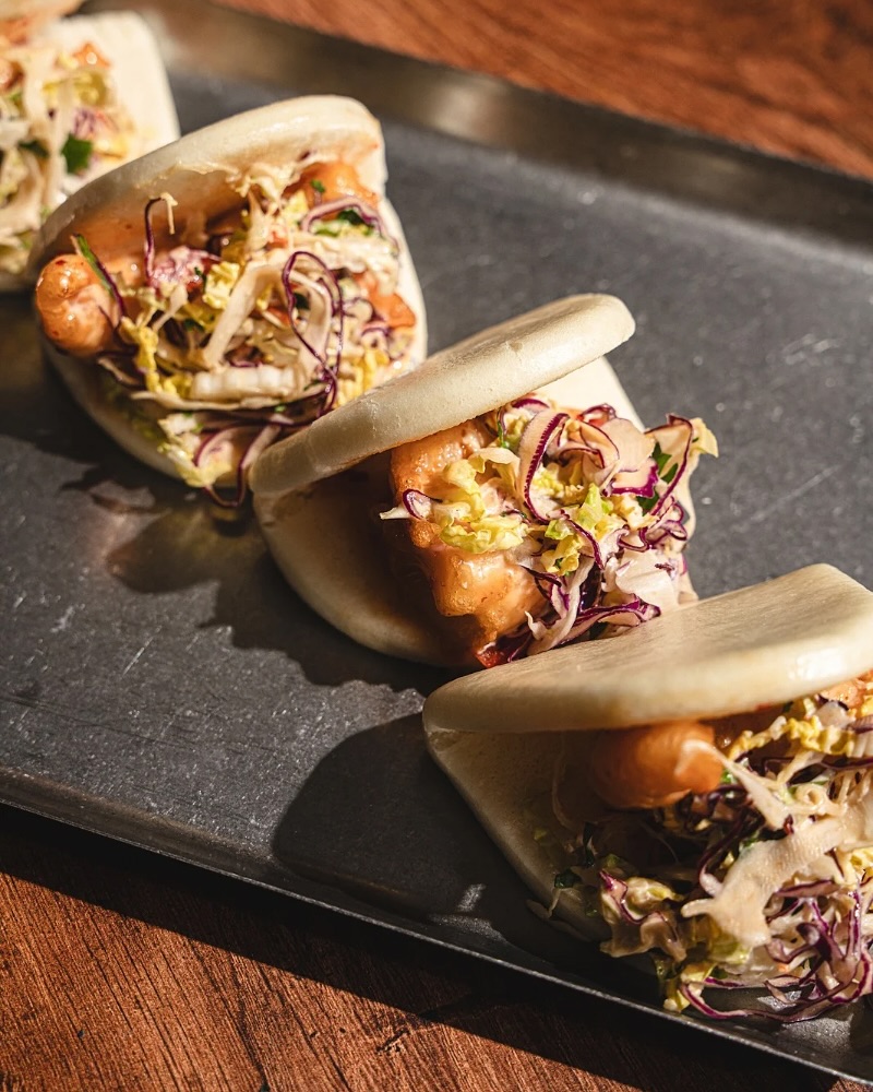 Several open bao buns with fried protein and coleslaw on tray.