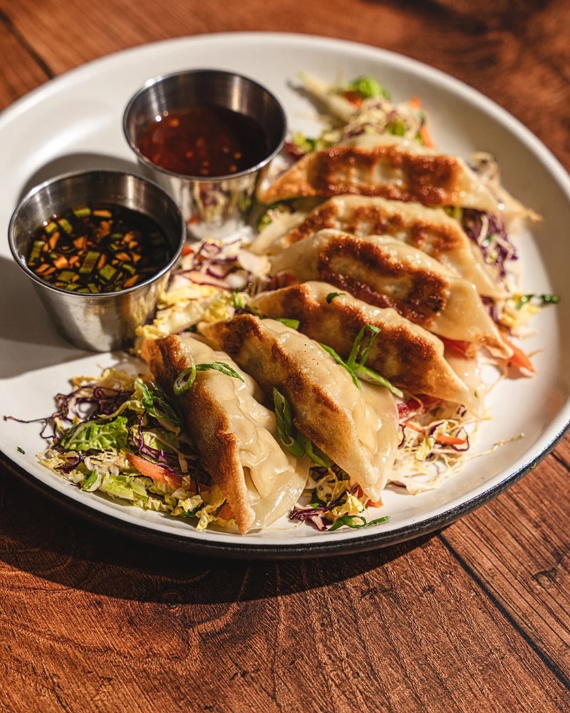 A plate of pan-fried dumplings, two sauces, and shredded cabbage.