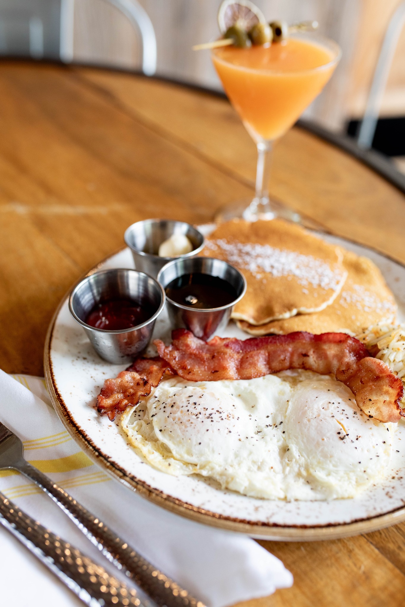 Breakfast plate with eggs, bacon, pancakes, and cocktail.