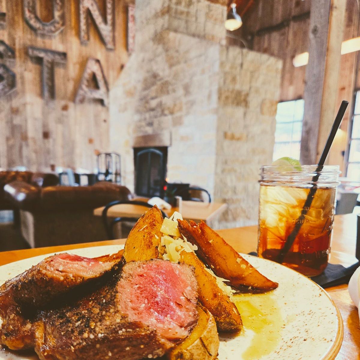 Steak, potato wedges, and a drink in a rustic restaurant setting.