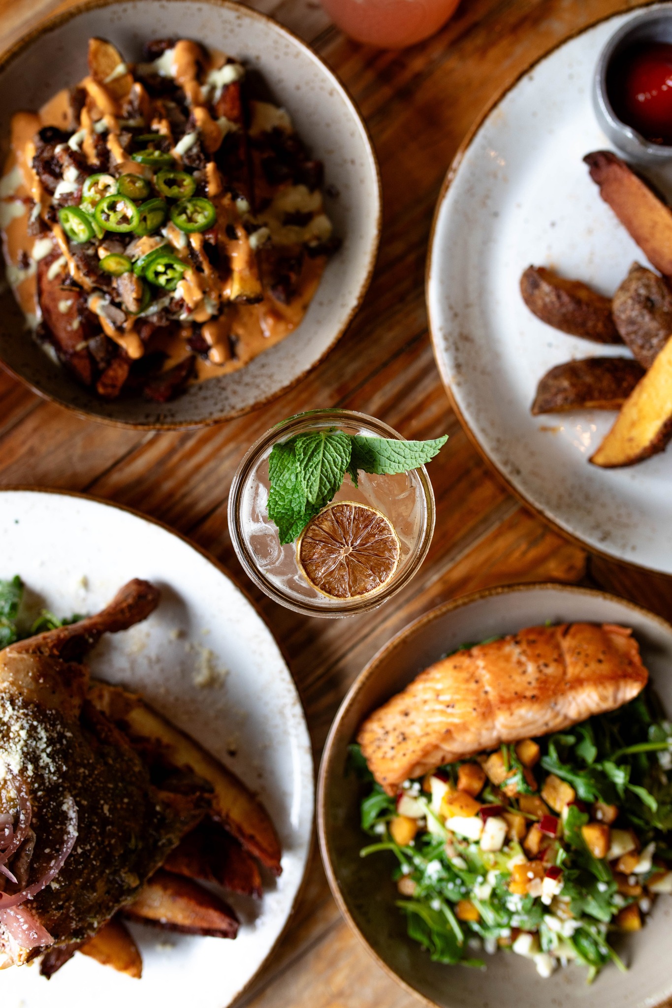 Four dinner plates and a cocktail on a wooden table, overhead view.