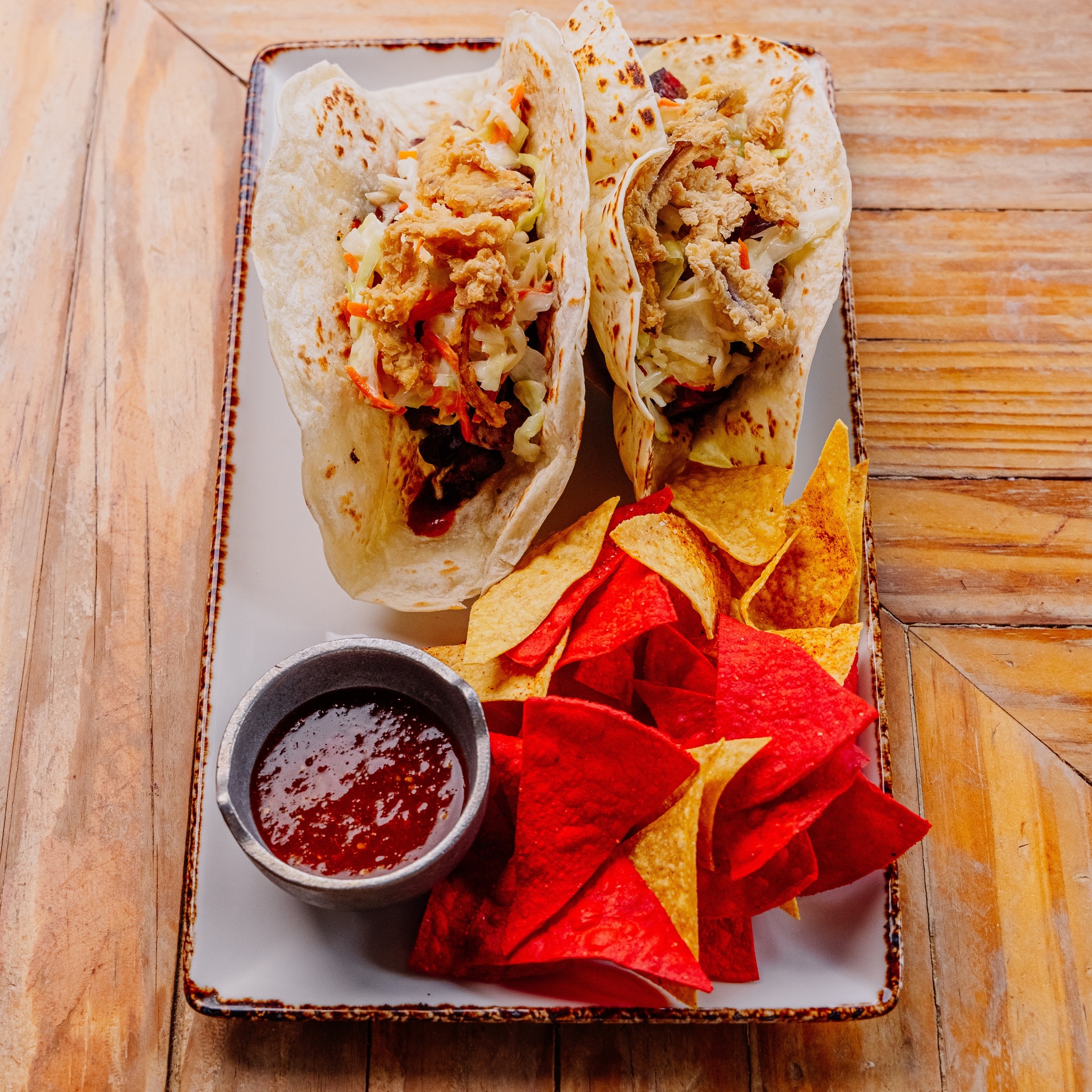 Two tacos, coleslaw, fried topping, red and yellow chips, and salsa.