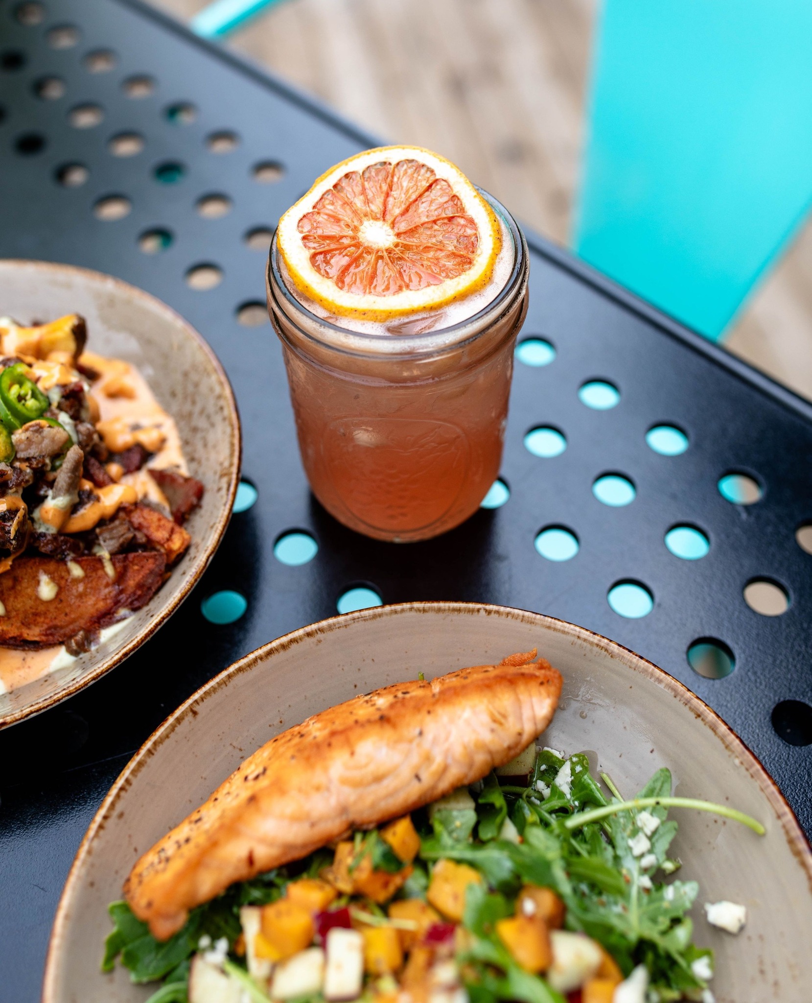 Grapefruit drink, salmon salad, and loaded potatoes on a black table.