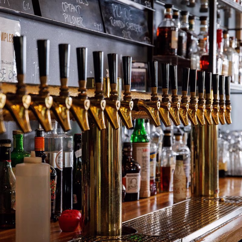 A long row of golden beer taps on a bar counter.
