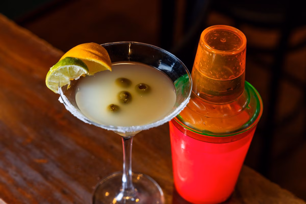 Salt-rimmed martini glass with olives, lime, orange peel, and shaker.
