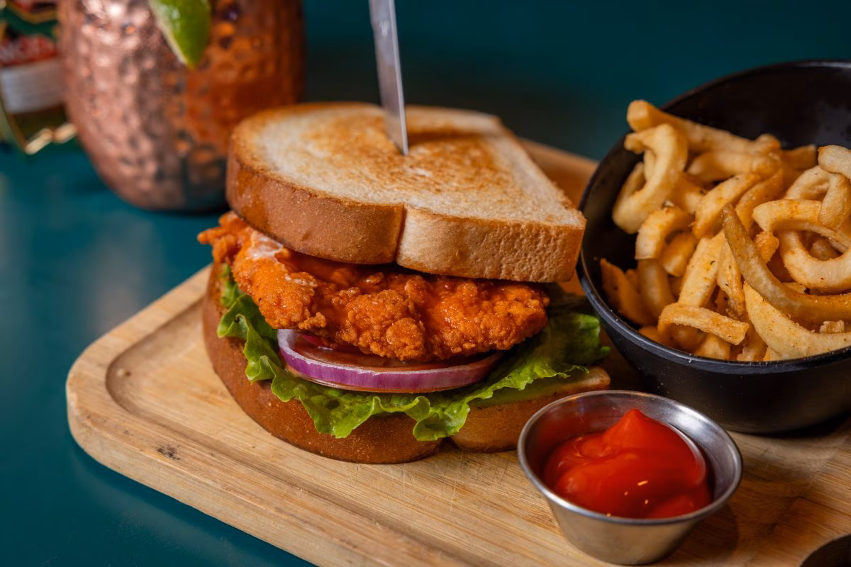 Fried chicken sandwich on toasted bread, with fries and ketchup.
