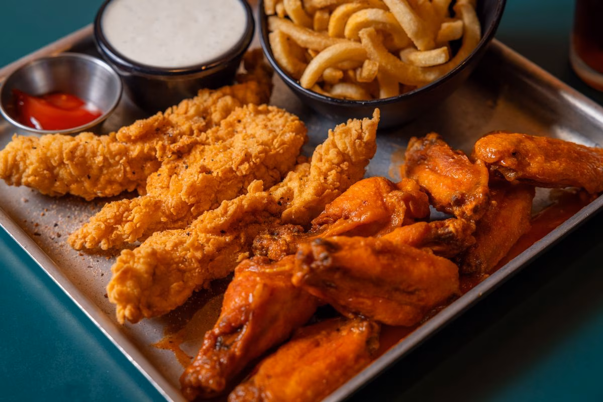Chicken tenders, buffalo wings, fries, and sauces on a metal tray.