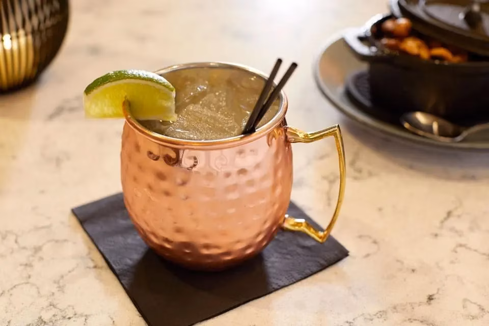 Drink in a hammered copper mug with lime, ice, and straws.