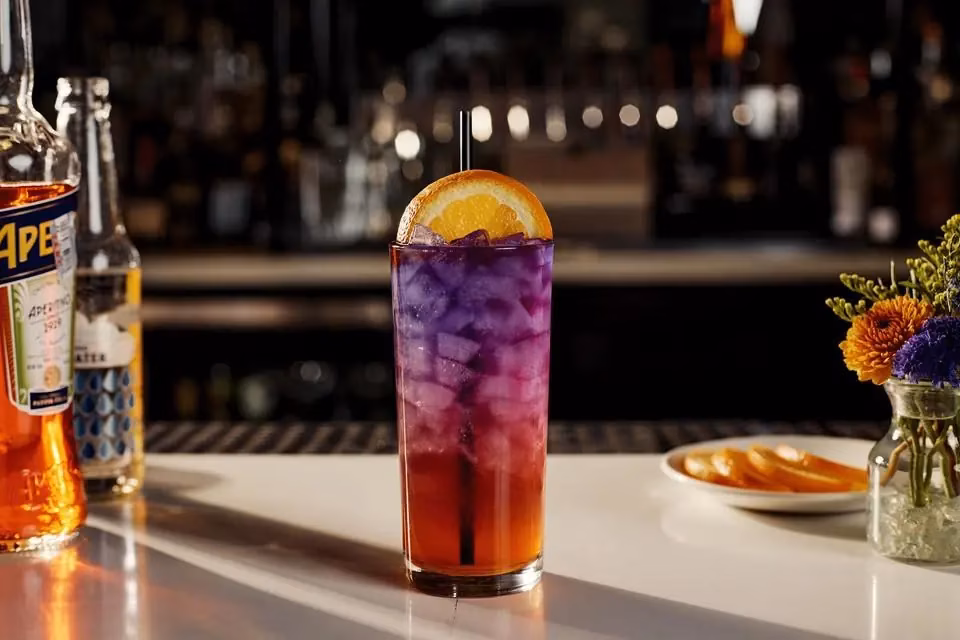 Orange and purple layered cocktail with an orange slice on a bar.