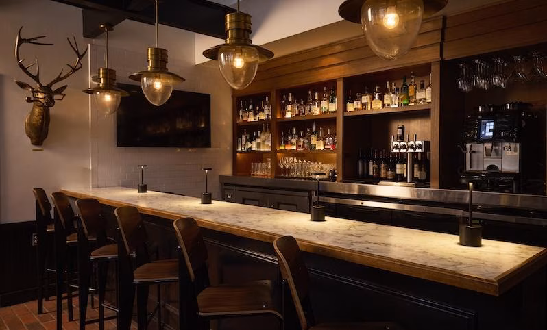 Bar with marble counter, hanging lights, bar stools, and liquor bottles.