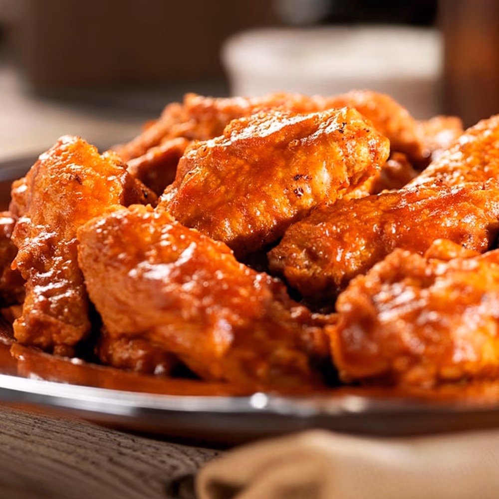 Glossy, red-orange coated chicken wings on a brown plate.