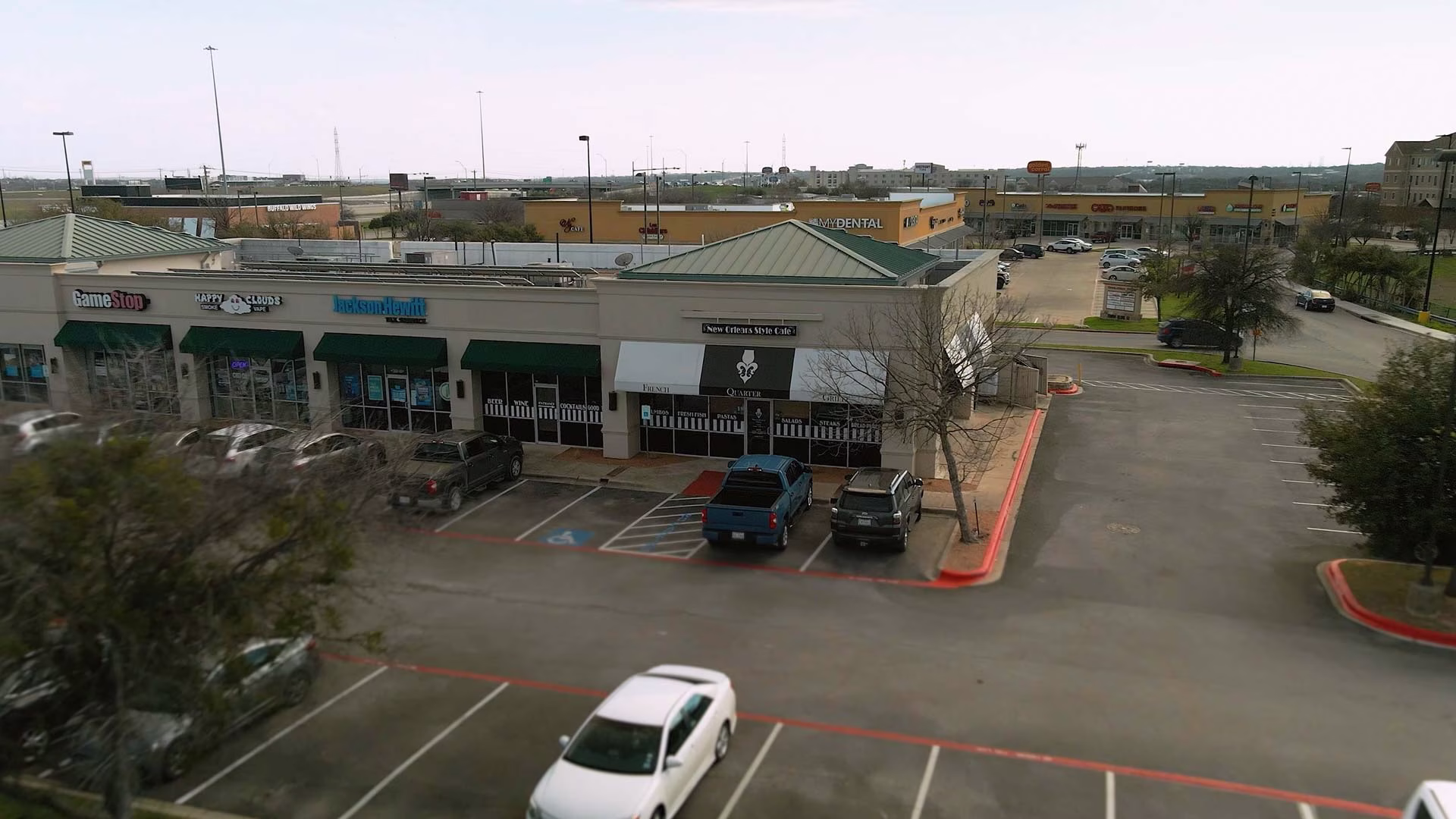 Strip mall with GameStop, Jackson Hewitt, New Orleans Style Cafe, and cars.