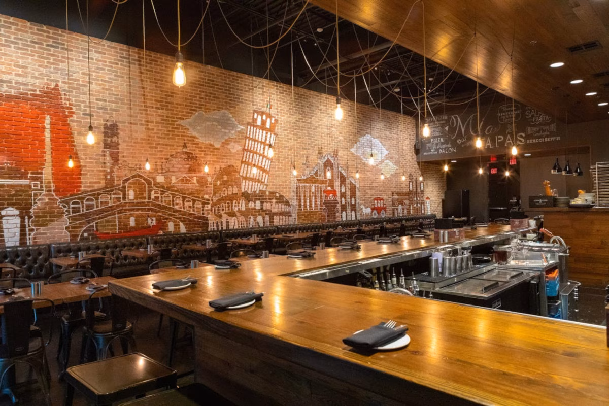 Restaurant interior featuring an Italian cityscape mural and a long wooden bar.