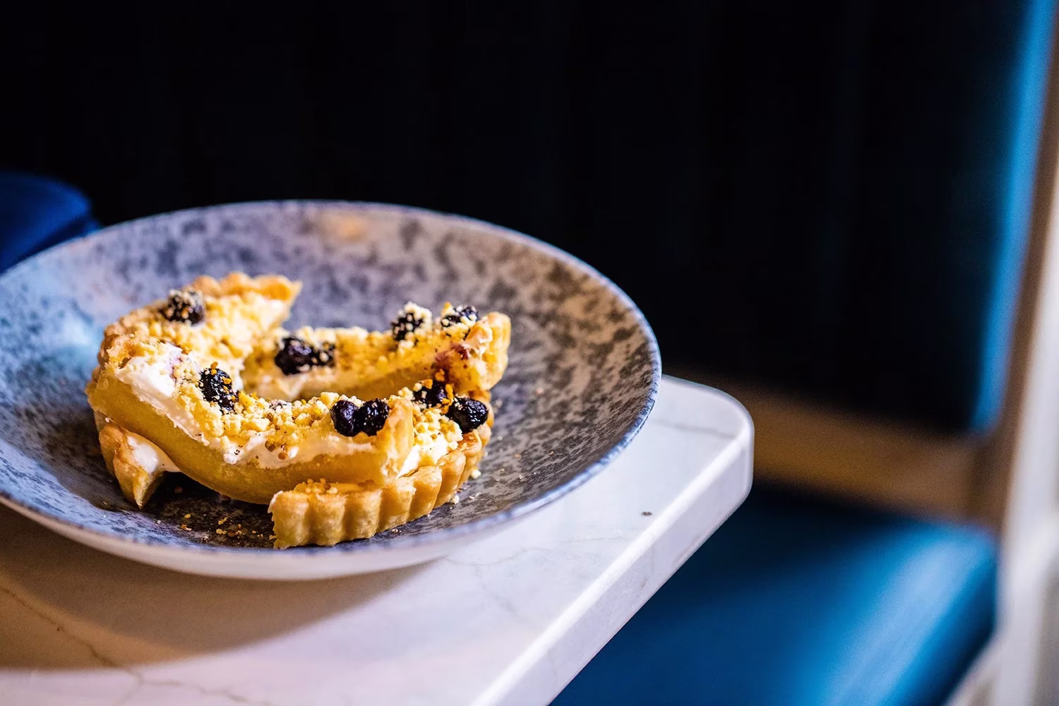 Two dessert tart pieces with cream, crumble, and berries on a plate.