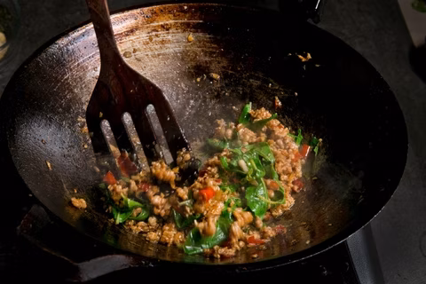 Ground meat and basil are stir-fried in a wok.