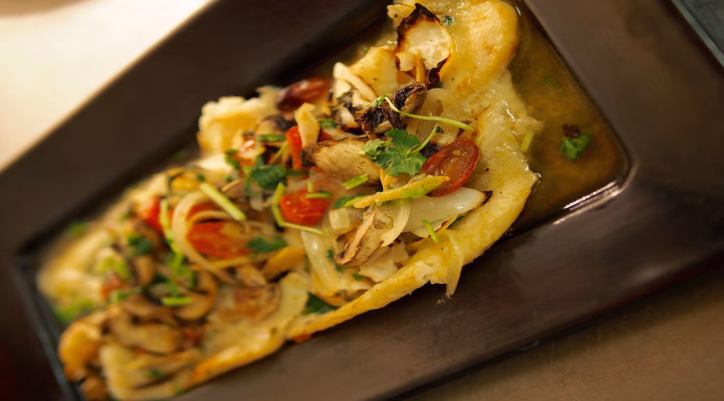 Dish with mushrooms, tomatoes, onions, and herbs in sauce on a plate.