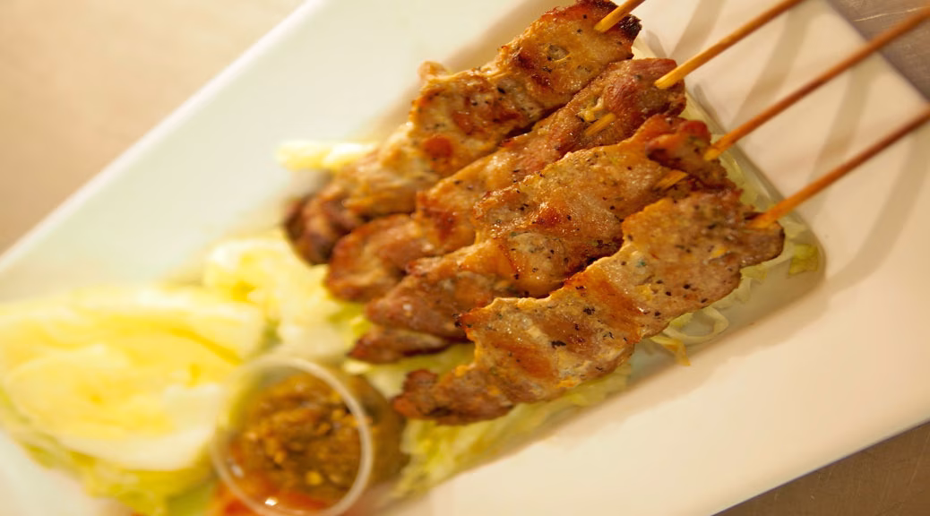 Four grilled meat skewers, shredded cabbage, and dipping sauce on a plate.
