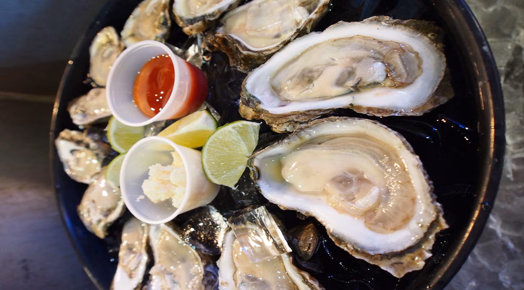 Raw oysters on the half shell with lime and sauces on ice.