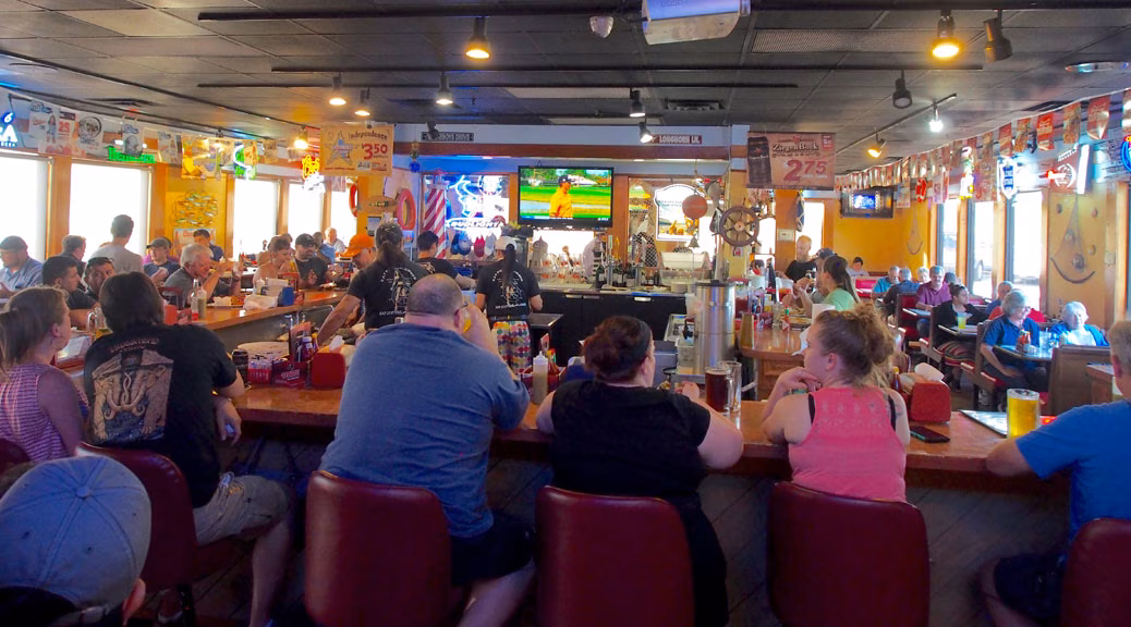 Busy bar and grill with patrons sitting at counter and tables.