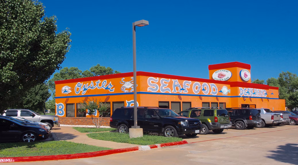 Orange "Oysters Seafood" restaurant building with cars in parking lot.