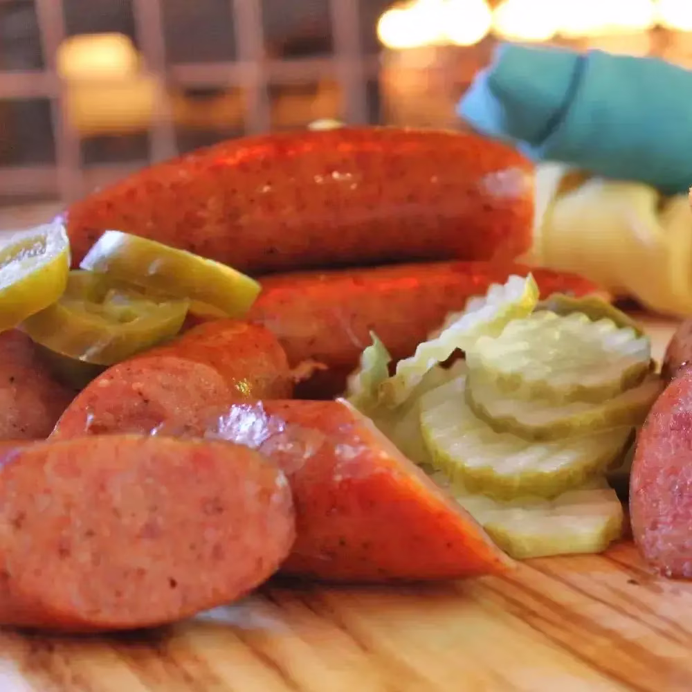 Sliced and whole sausages with pickles and jalapeños on wood.