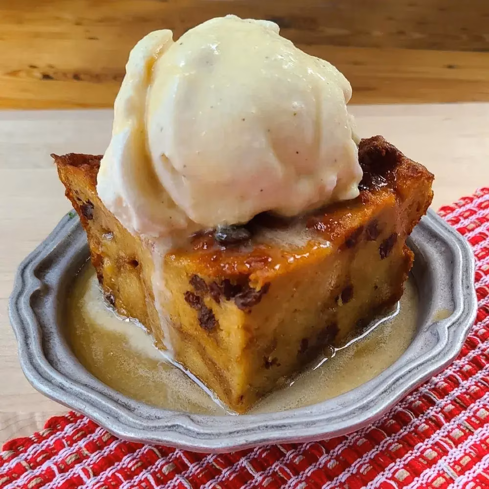 Bread pudding with dark inclusions, melting vanilla ice cream, and sauce.