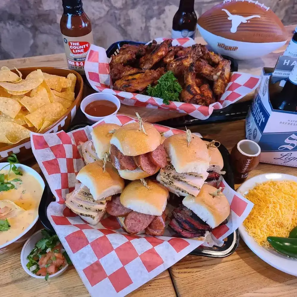Assorted BBQ sliders, chicken wings, nachos, beer, and a football.