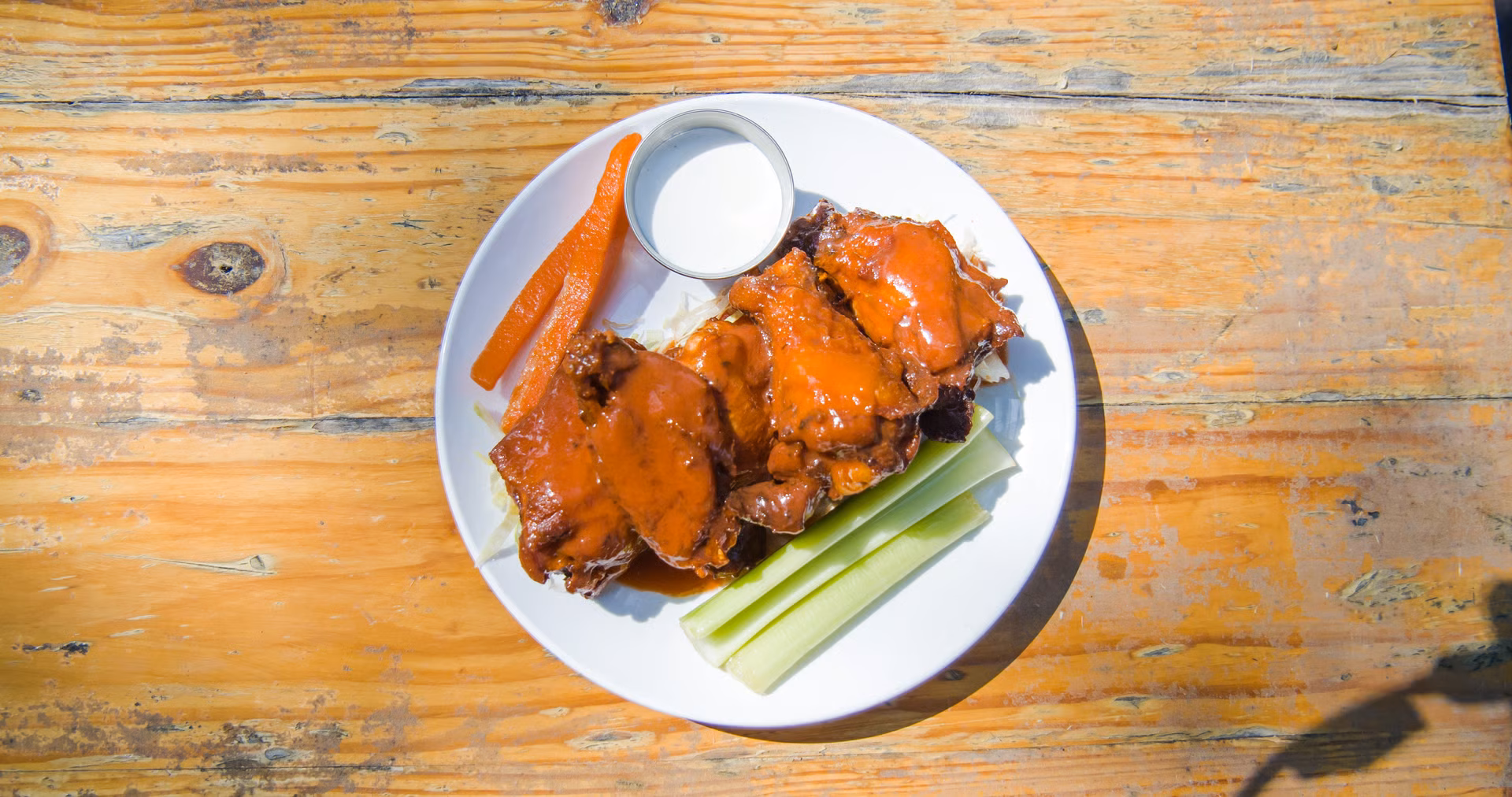 Chicken wings, carrots, celery, and a cup of dipping sauce on wood.