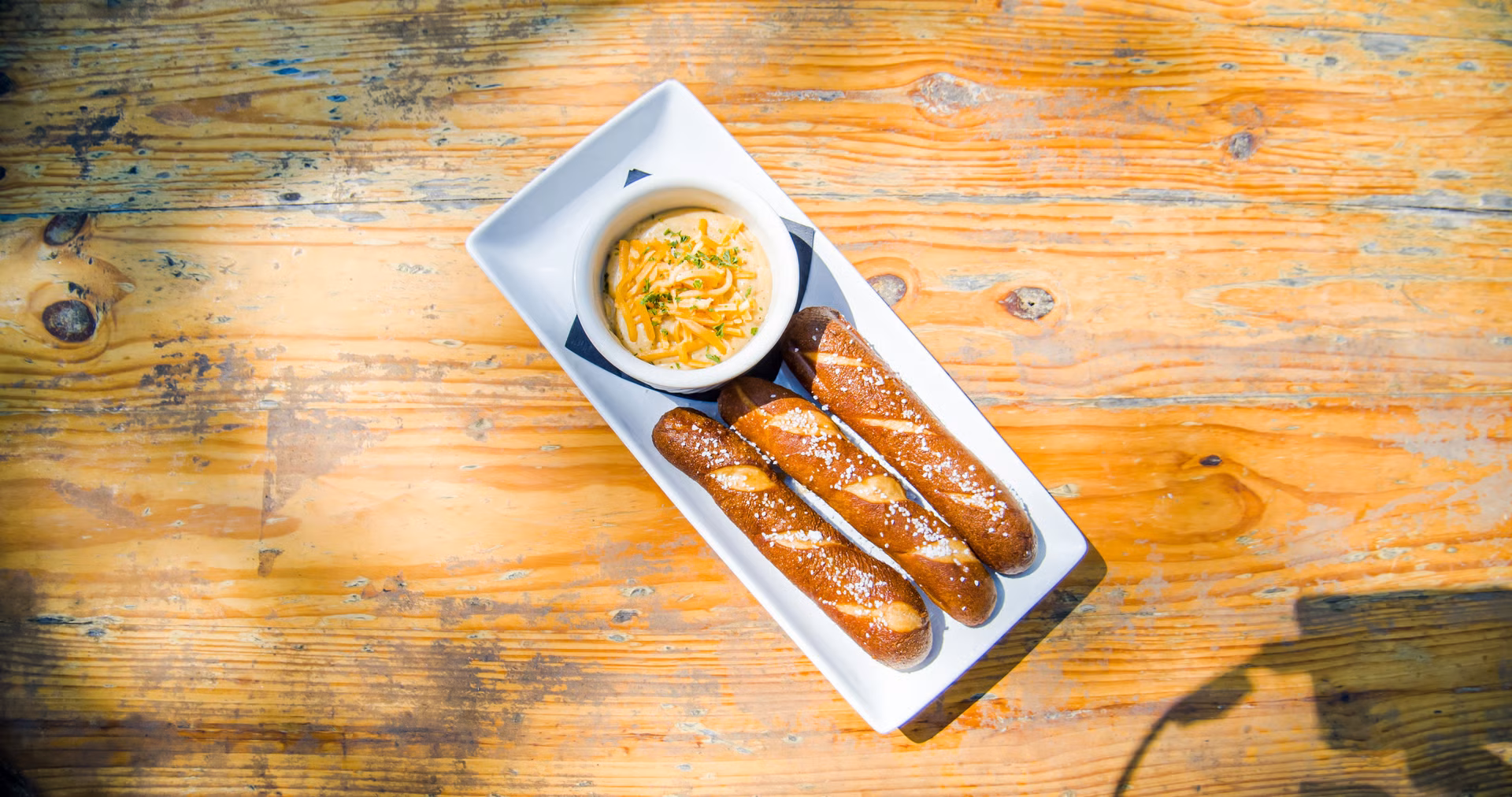 Three salted pretzel sticks and a cheese dip on a wooden table.